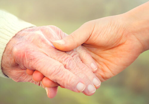 Elderly woman holding hands with young caretaker